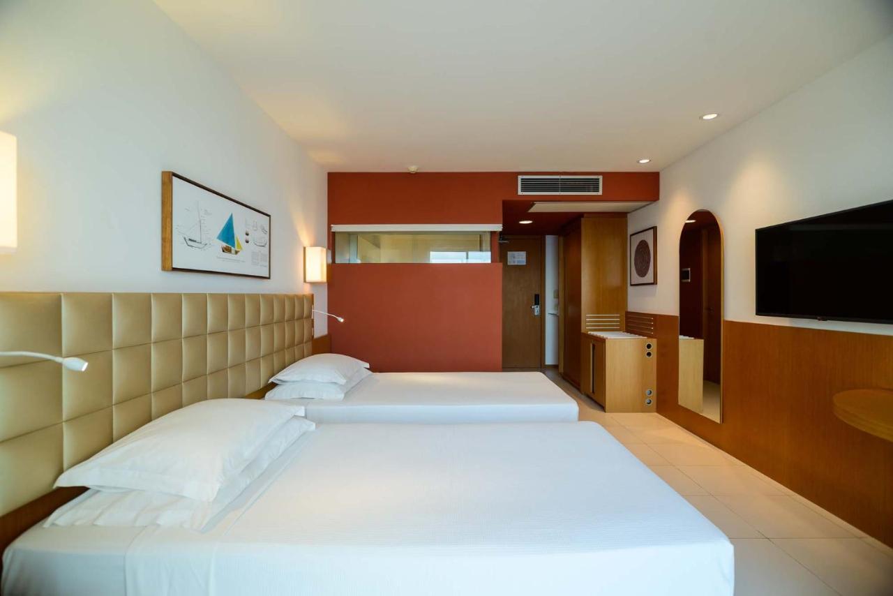 Hotel Luzeiros Sao Luis Extérieur photo The image shows a modern hotel room featuring two single beds with white bedding. The headboard of the beds is a soft, cream-colored material. The room has a minimalist design with light-colored walls and a contrasting accent wall in a warm orange sh