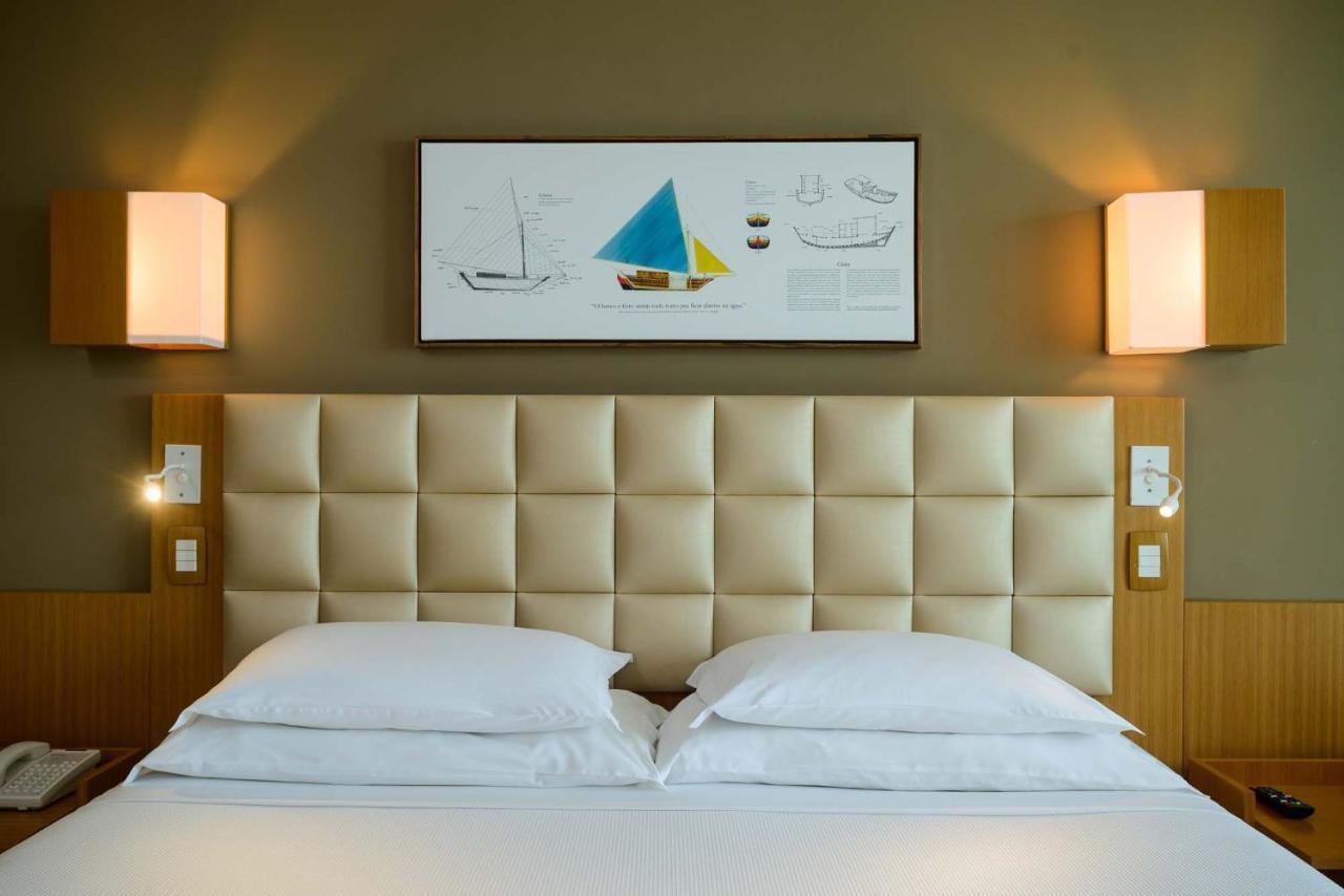Hotel Luzeiros Sao Luis Extérieur photo The photo shows a modern hotel room with a neatly made bed consisting of two white pillows. The headboard of the bed is upholstered in a light, padded material. Above the bed, there is a framed artwork featuring colorful sailboat illustrations, inclu