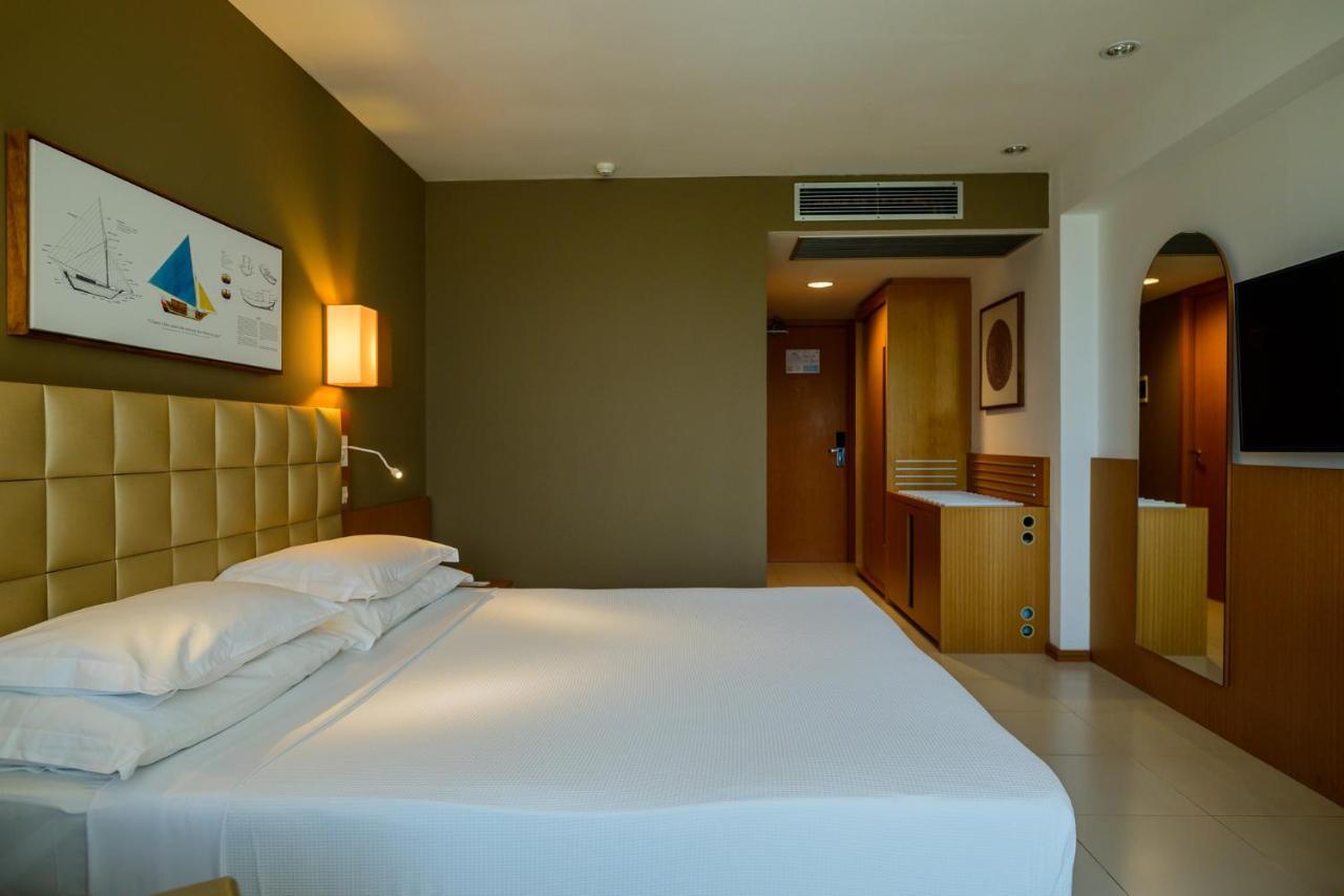 Hotel Luzeiros Sao Luis Extérieur photo The photo shows a modern hotel room with a simple and elegant design. The room features a large bed with white linens, positioned against a beige upholstered headboard. There is a bedside lamp on one side of the bed. The walls are in soft shades, wit