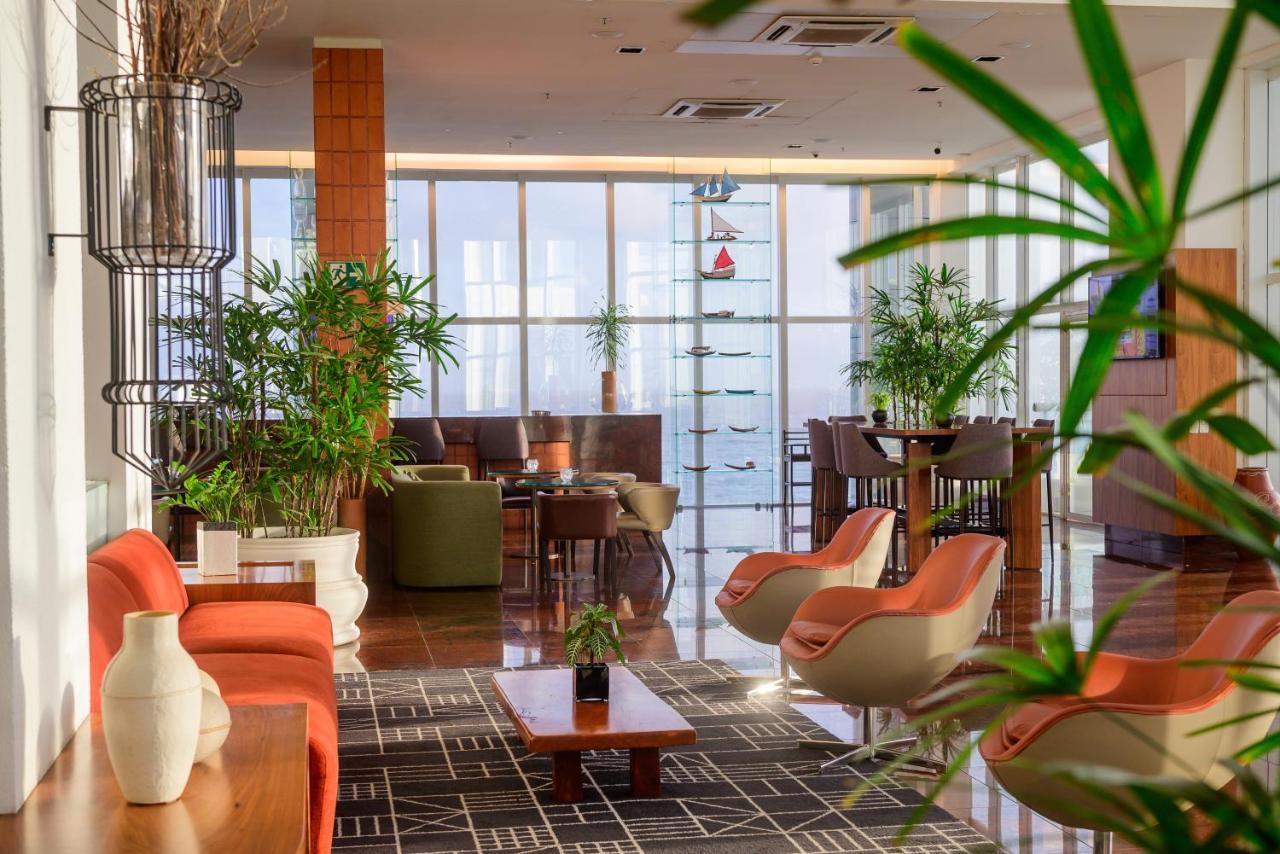 Hotel Luzeiros Sao Luis Extérieur photo The photo shows a modern, stylish indoor lounge area with a bright and airy atmosphere. There are several seating arrangements, including chairs with orange upholstery and green sofas. A wooden coffee table is centered on a patterned rug. The space f