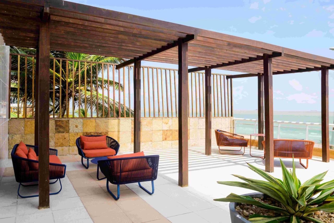 Hotel Luzeiros Sao Luis Extérieur photo The photo shows a modern outdoor seating area under a wooden pergola. There are several comfortable chairs with orange cushions arranged around a small table. The backdrop features a tropical setting with palm trees and possibly a body of water visib
