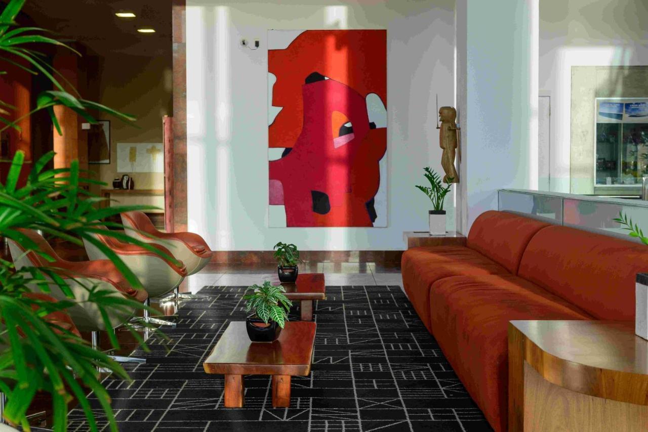 Hotel Luzeiros Sao Luis Extérieur photo The photo depicts a modern interior space, likely a lounge or living area. In the foreground, there is a large orange sofa complemented by two small wooden coffee tables, each adorned with potted plants. The floor features a black and white patterned