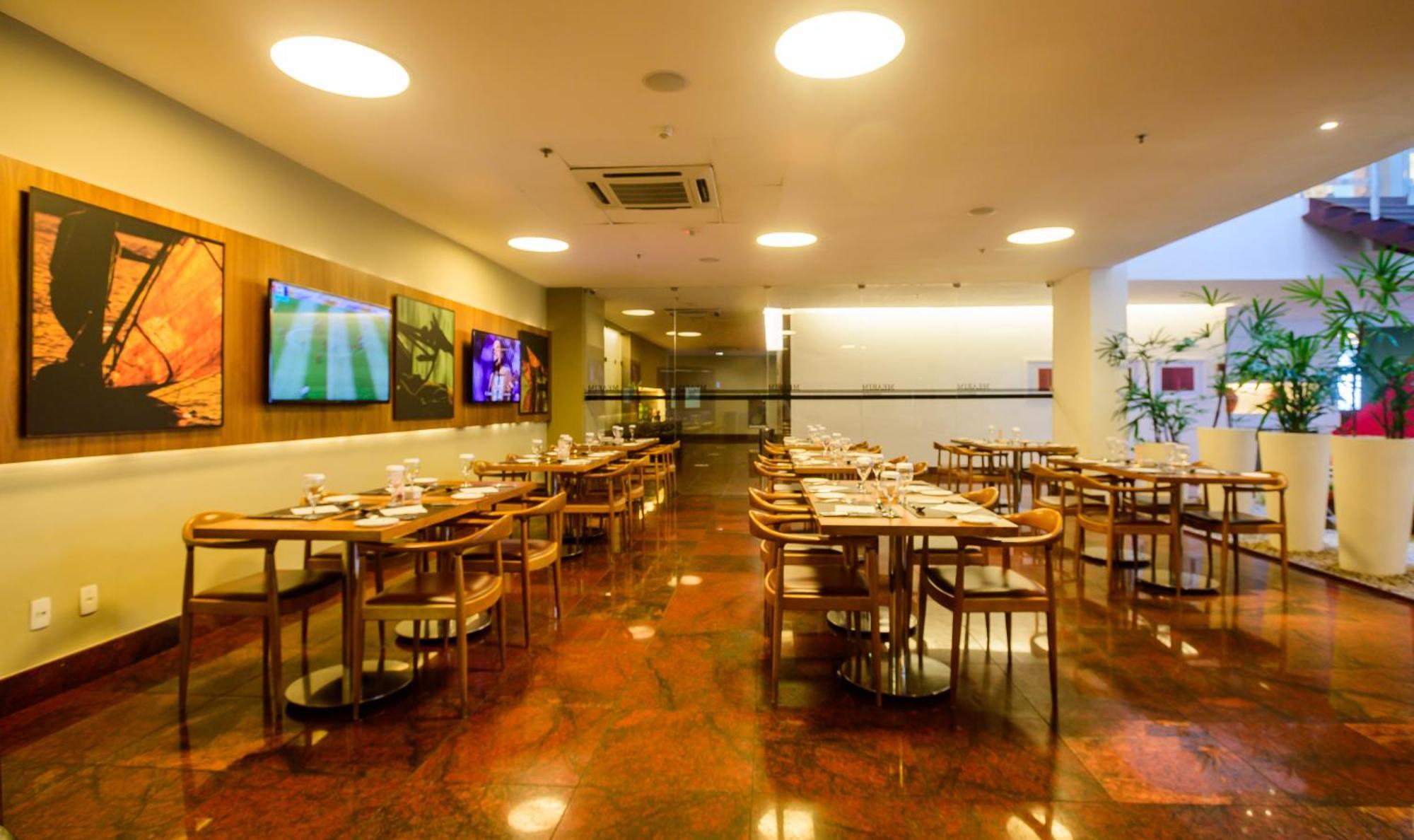 Hotel Luzeiros Sao Luis Extérieur photo The image shows the interior of a restaurant. The space features several wooden tables and chairs arranged throughout, with table settings visible on each table. The flooring appears to be polished and reflective, possibly with a reddish-brown tone. 