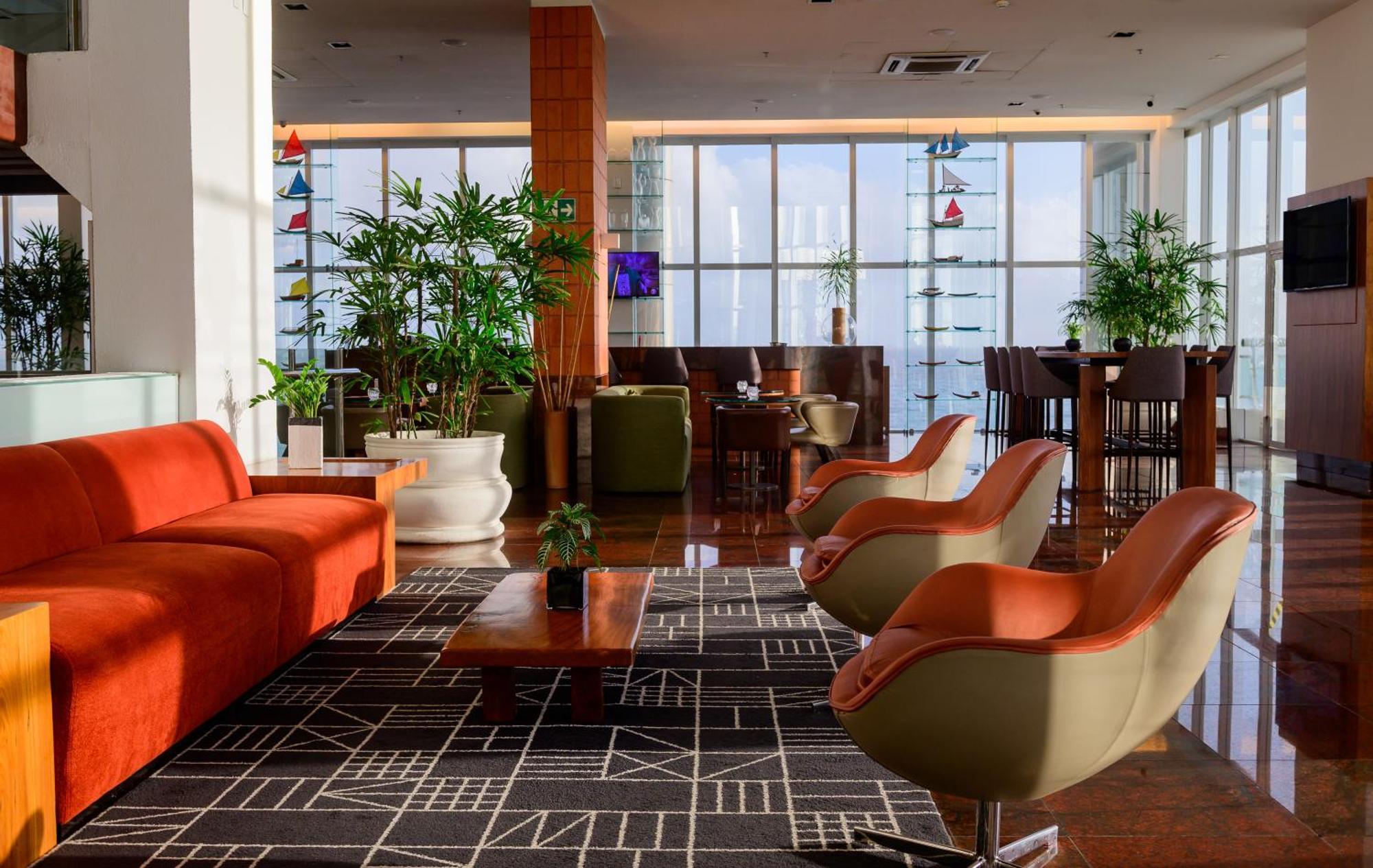 Hotel Luzeiros Sao Luis Extérieur photo The photo shows a modern lounge area with large windows allowing natural light to flood in. There is an orange couch and stylish green and orange chairs arranged around a coffee table. The floor features a geometric patterned rug, and there are sever