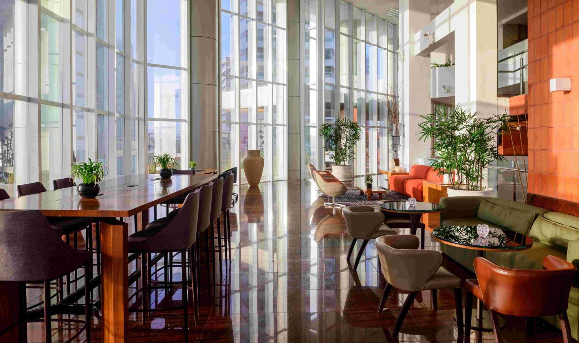 Hotel Luzeiros Sao Luis Extérieur photo The photo shows a modern, stylish interior space, likely a lounge or lobby area. It features large glass windows that allow abundant natural light to fill the room, illuminating the polished floor. The space includes a long bar table with stools, as 