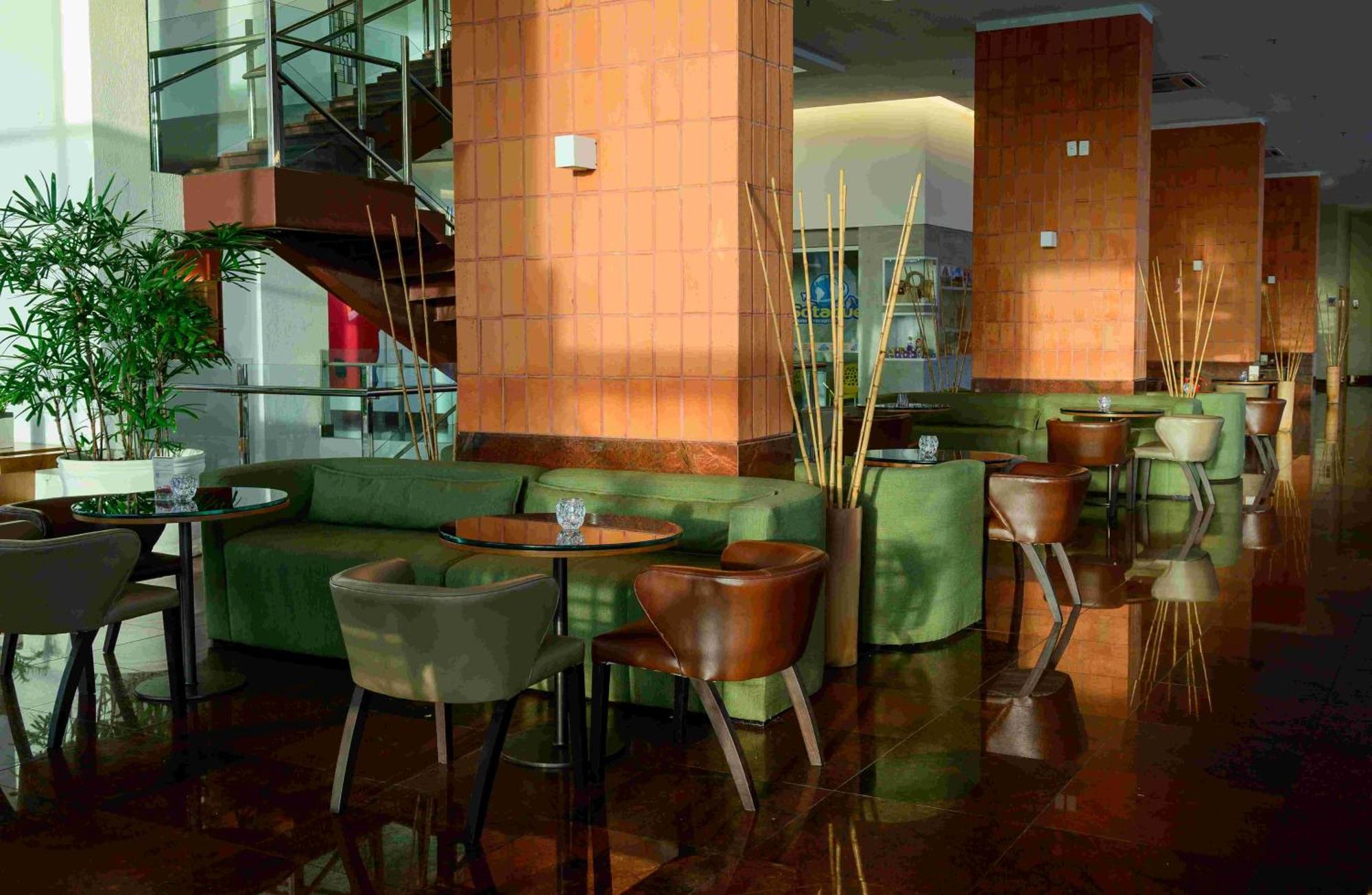 Hotel Luzeiros Sao Luis Extérieur photo The photo shows a modern, stylish interior of a café or lounge. There's a mix of seating arrangements, including green sofas and wooden chairs around small tables. The space has large windows that let in natural light, highlighting the glossy floor a