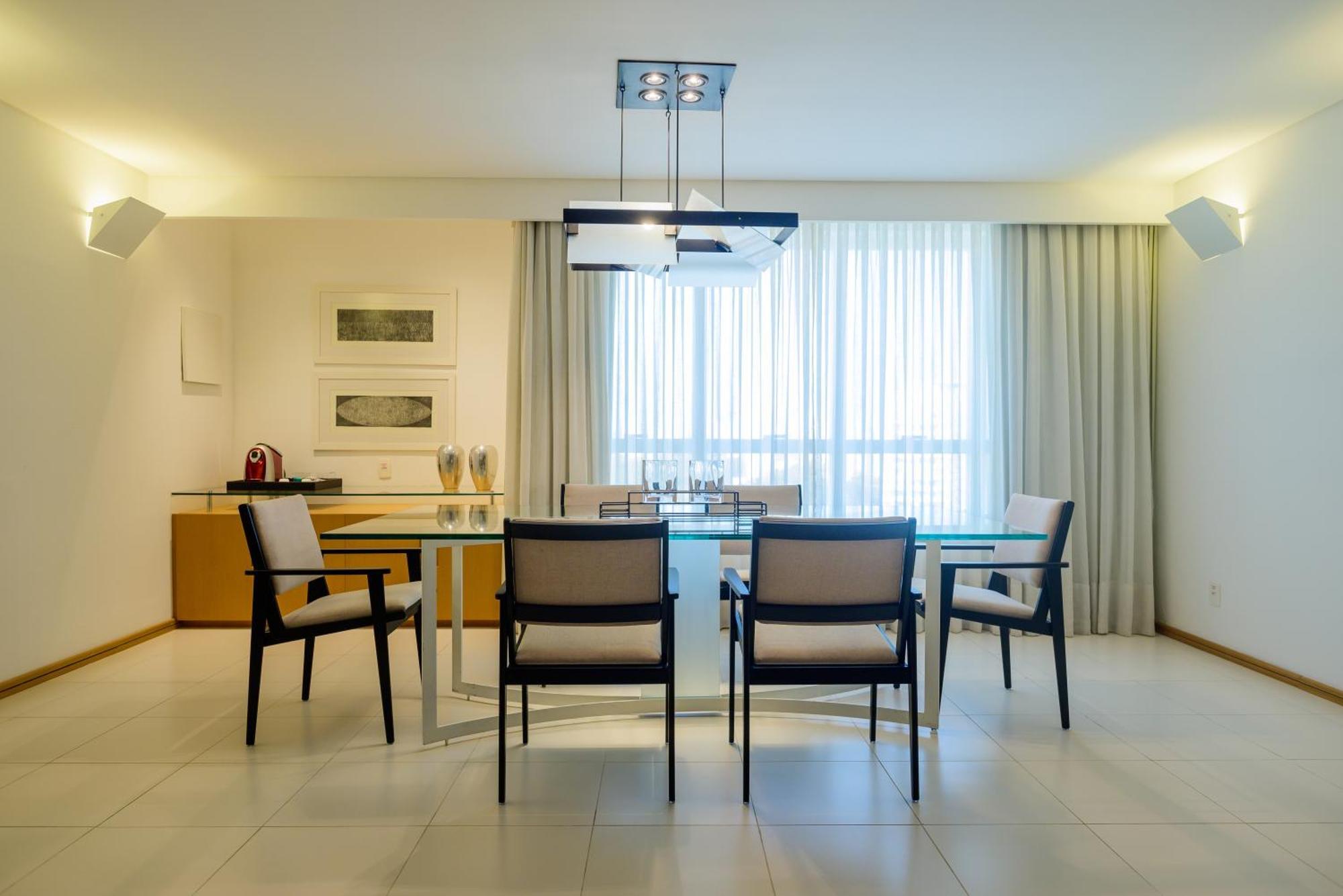 Hotel Luzeiros Sao Luis Extérieur photo The photo shows a modern dining area with a stylish table and four chairs. The table has a glass top and is situated under a contemporary light fixture. Behind the table is a sideboard or cabinet, and the space features large windows that provide nat