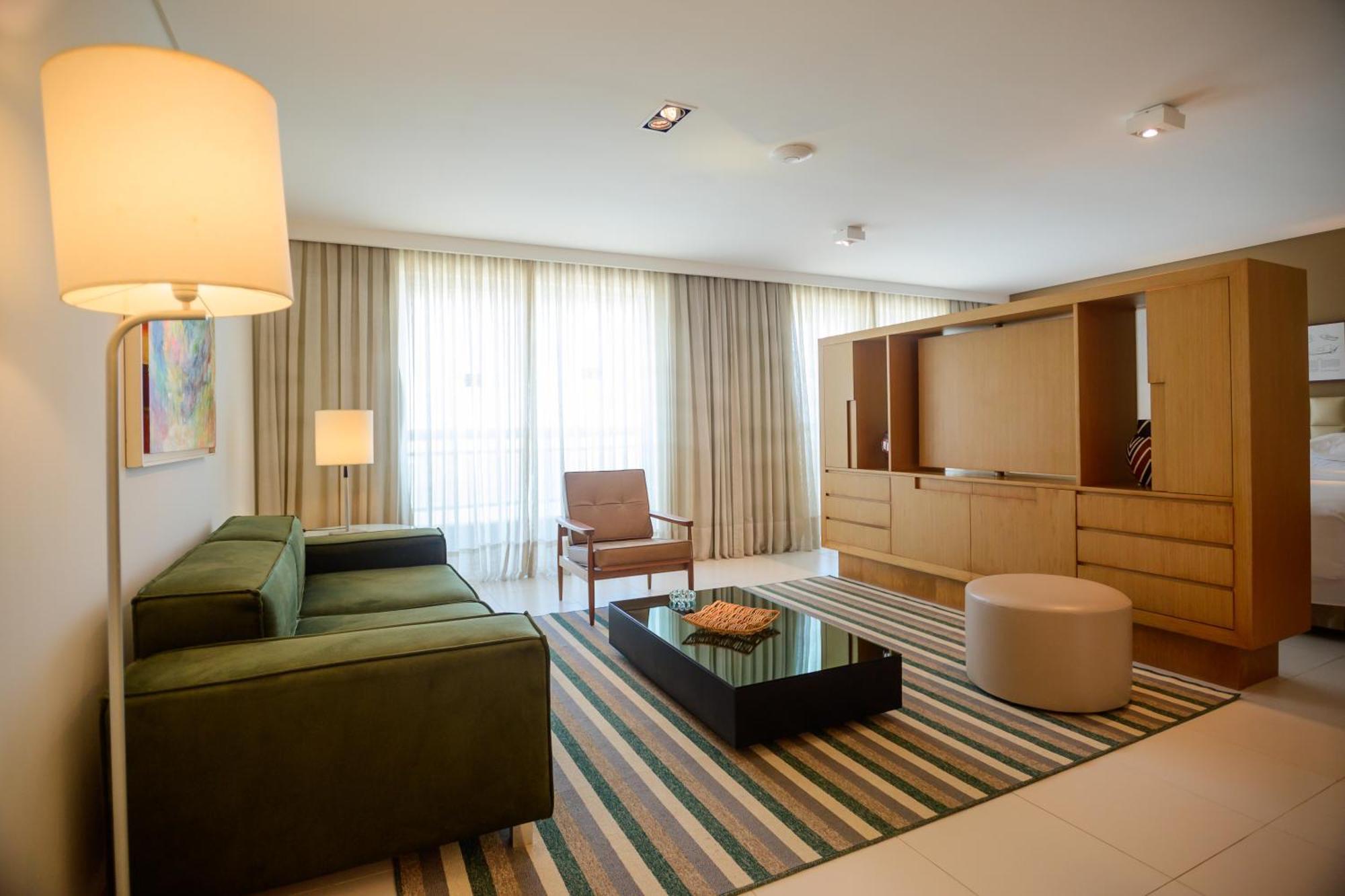 Hotel Luzeiros Sao Luis Extérieur photo The photo shows a modern living room with a clean and minimalist design. There is a green sectional sofa positioned against one wall, complemented by a brown armchair nearby. A coffee table with a black surface sits in the center of the room, with a 
