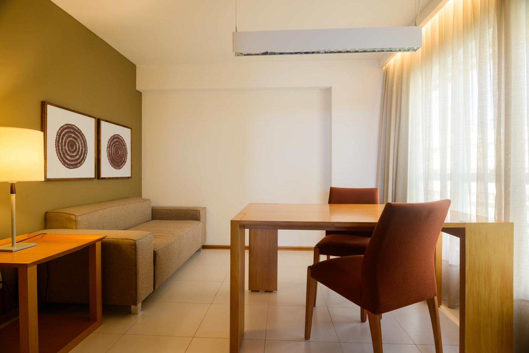 Hotel Luzeiros Sao Luis Extérieur photo The photo shows an interior space that appears to be a small living or dining area. On the left side, there is a brown sofa, and across from it, a light wooden dining table with two orange-brown chairs. The walls are painted in a soft green color, an