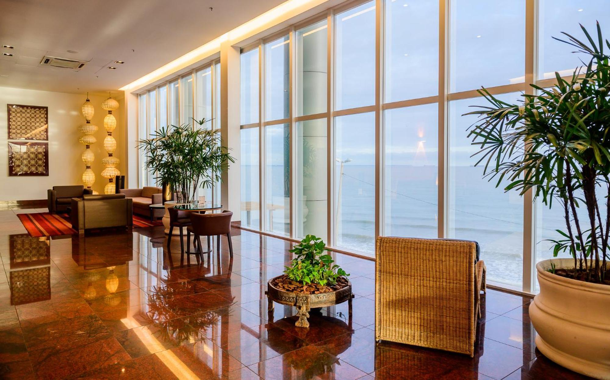 Hotel Luzeiros Sao Luis Extérieur photo The photo depicts a modern interior space, likely a lounge or atrium, featuring large windows that offer a view of the ocean. The room is elegantly furnished with a mix of seating options, including a wicker chair and tables. Indoor plants are presen