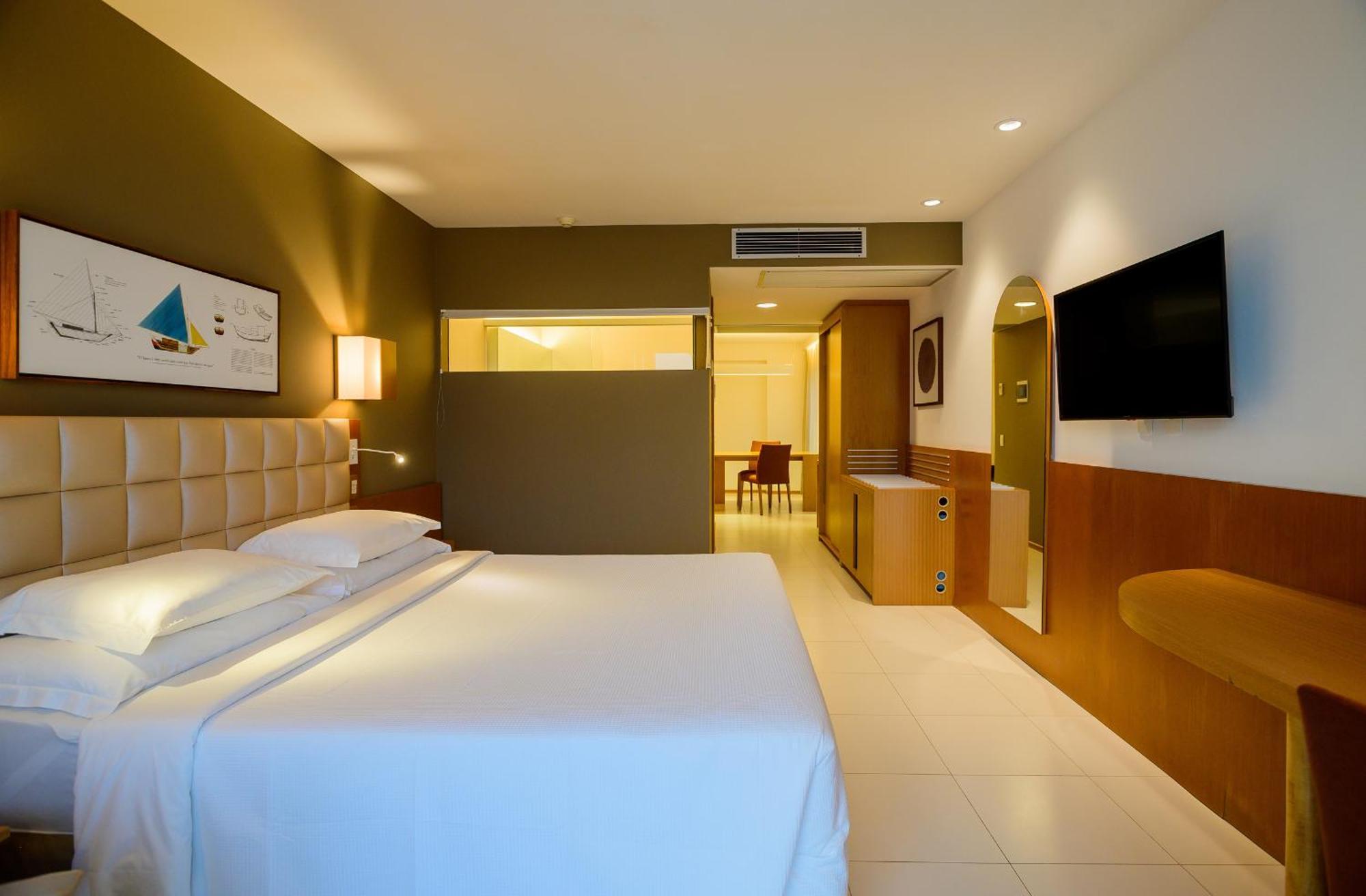Hotel Luzeiros Sao Luis Extérieur photo The photo shows a modern hotel room featuring a neatly made bed with white linens. The room has neutral-colored walls, including a dark green accent wall. There is a piece of artwork above the bed, depicting a sailboat scene. To the right, a flat-scr