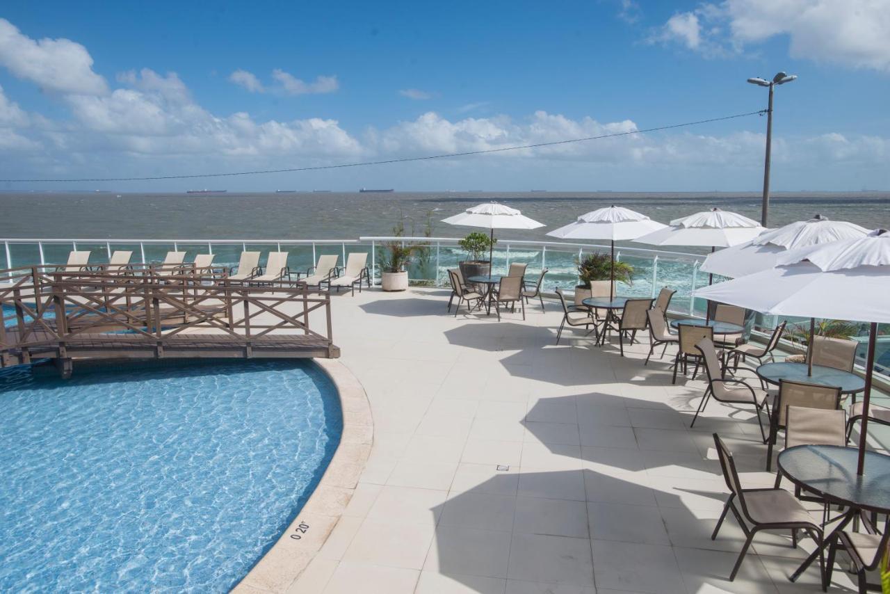 Hotel Luzeiros Sao Luis Extérieur photo The photo shows a pool area with a clear blue swimming pool surrounded by a deck. There are several lounge chairs and tables set up with umbrellas, providing shade. In the background, you can see the water beyond the pool, likely an ocean or large bo