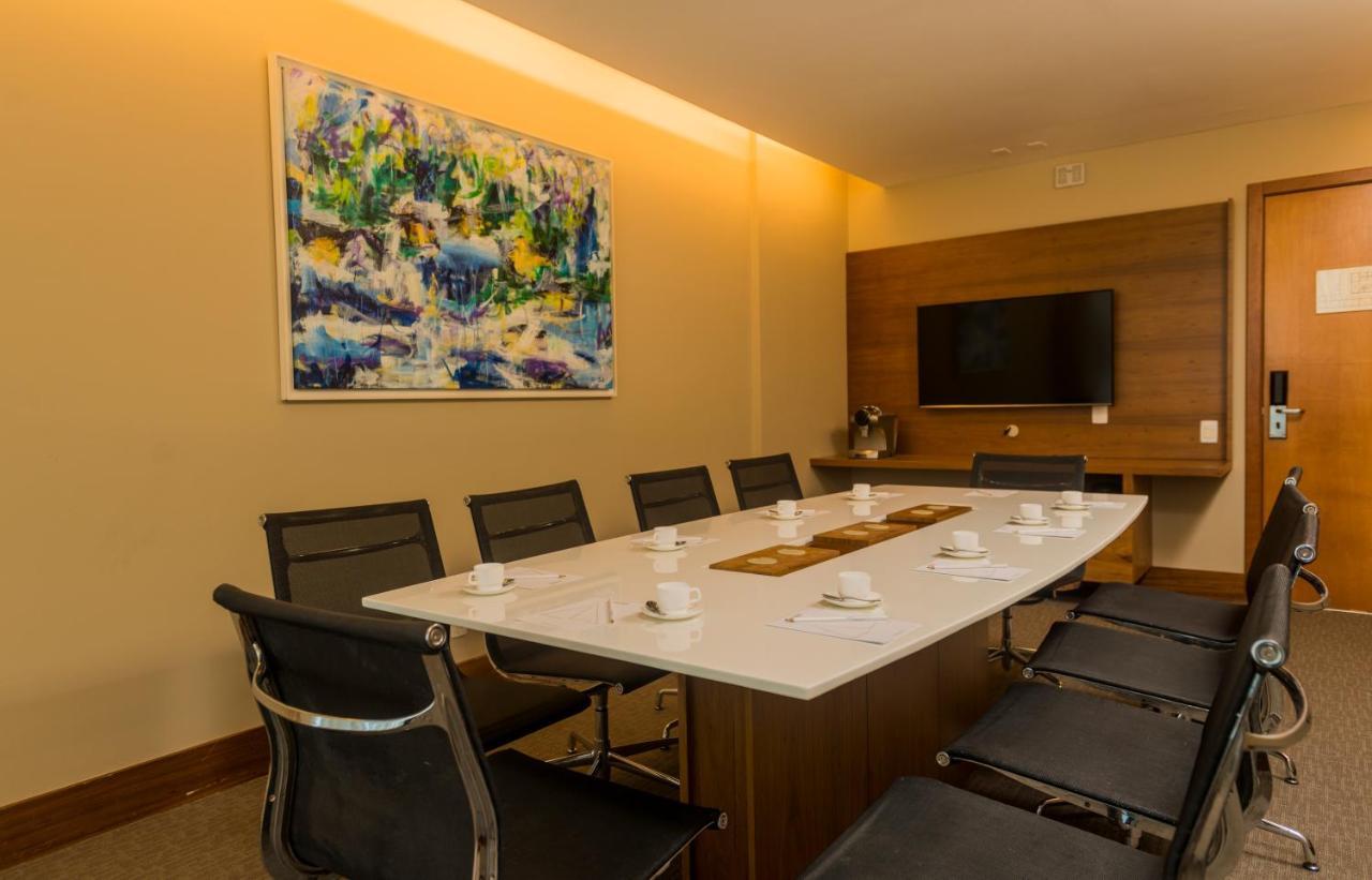 Hotel Luzeiros Sao Luis Extérieur photo The photo shows a modern conference room. It features a long rectangular table surrounded by eight black chairs. On the table, there are several small white cups and a decorative runner. The room is illuminated with soft lighting, and there is a larg