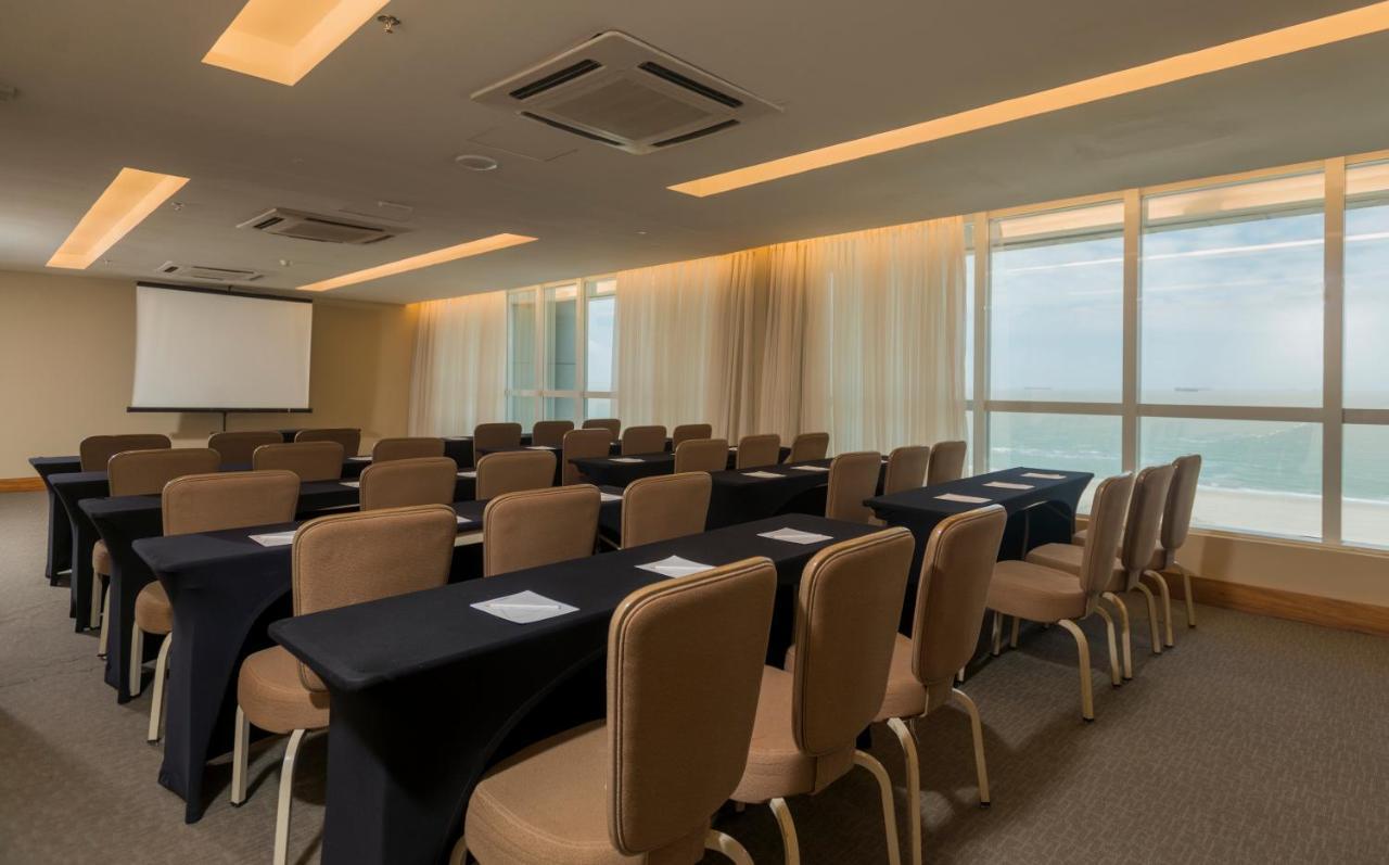 Hotel Luzeiros Sao Luis Extérieur photo The photo shows a meeting or conference room. There are rows of rectangular tables covered with black tablecloths, each accompanied by beige chairs. A screen for presentations is visible at the front of the room, and large windows let in natural ligh